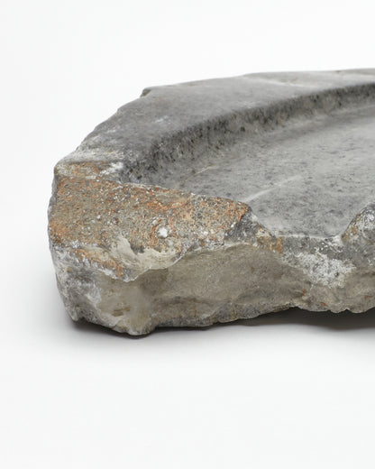 Angled close-up: organic-shaped gray stone tray with raw edges, flecks, subtle veining.