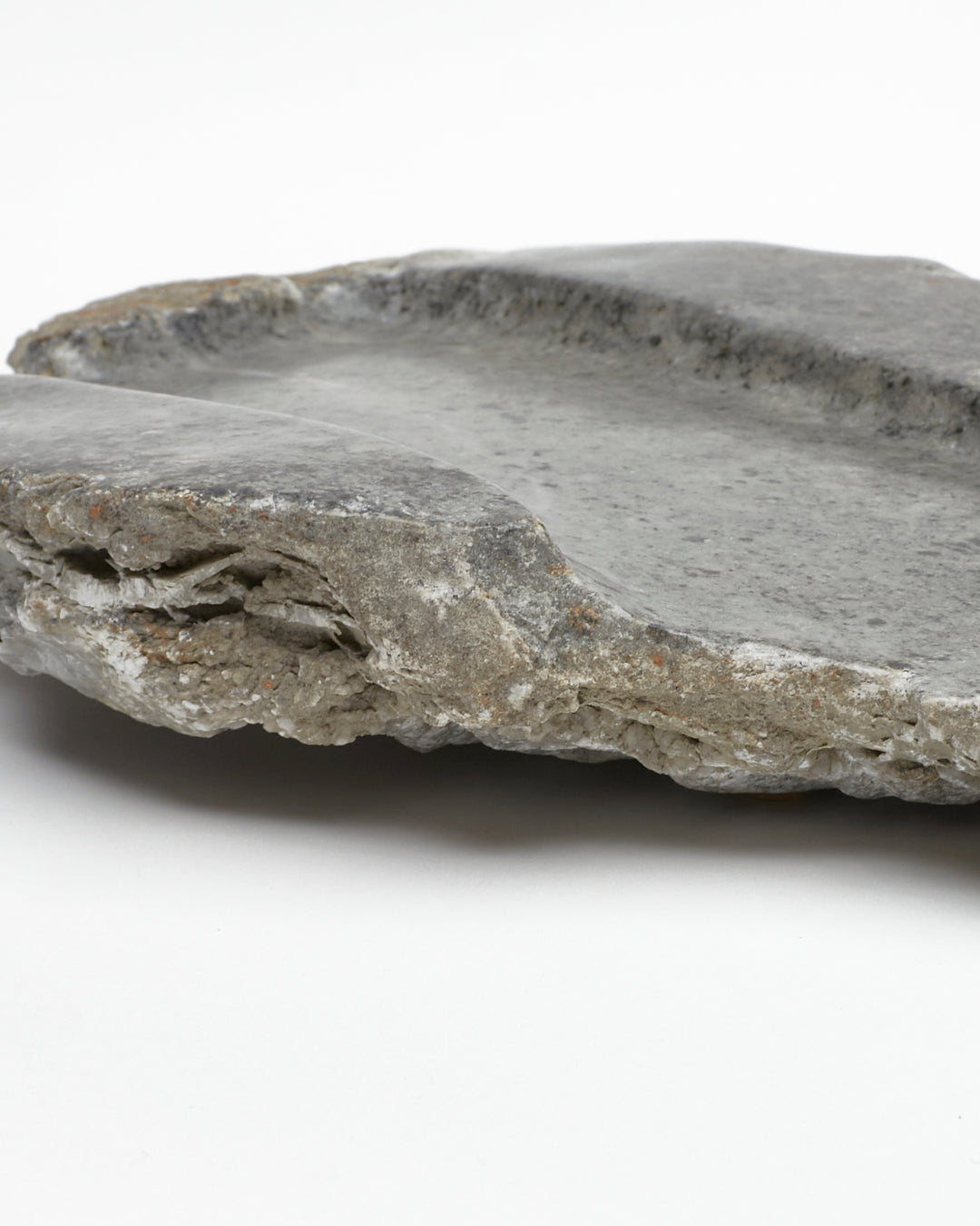 Close-up side view: organic-shaped gray stone tray with raw edges, brown and white flecks.