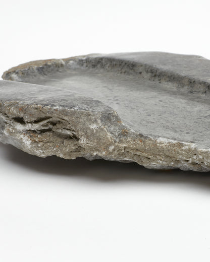 Close-up side view: organic-shaped gray stone tray with raw edges, brown and white flecks.