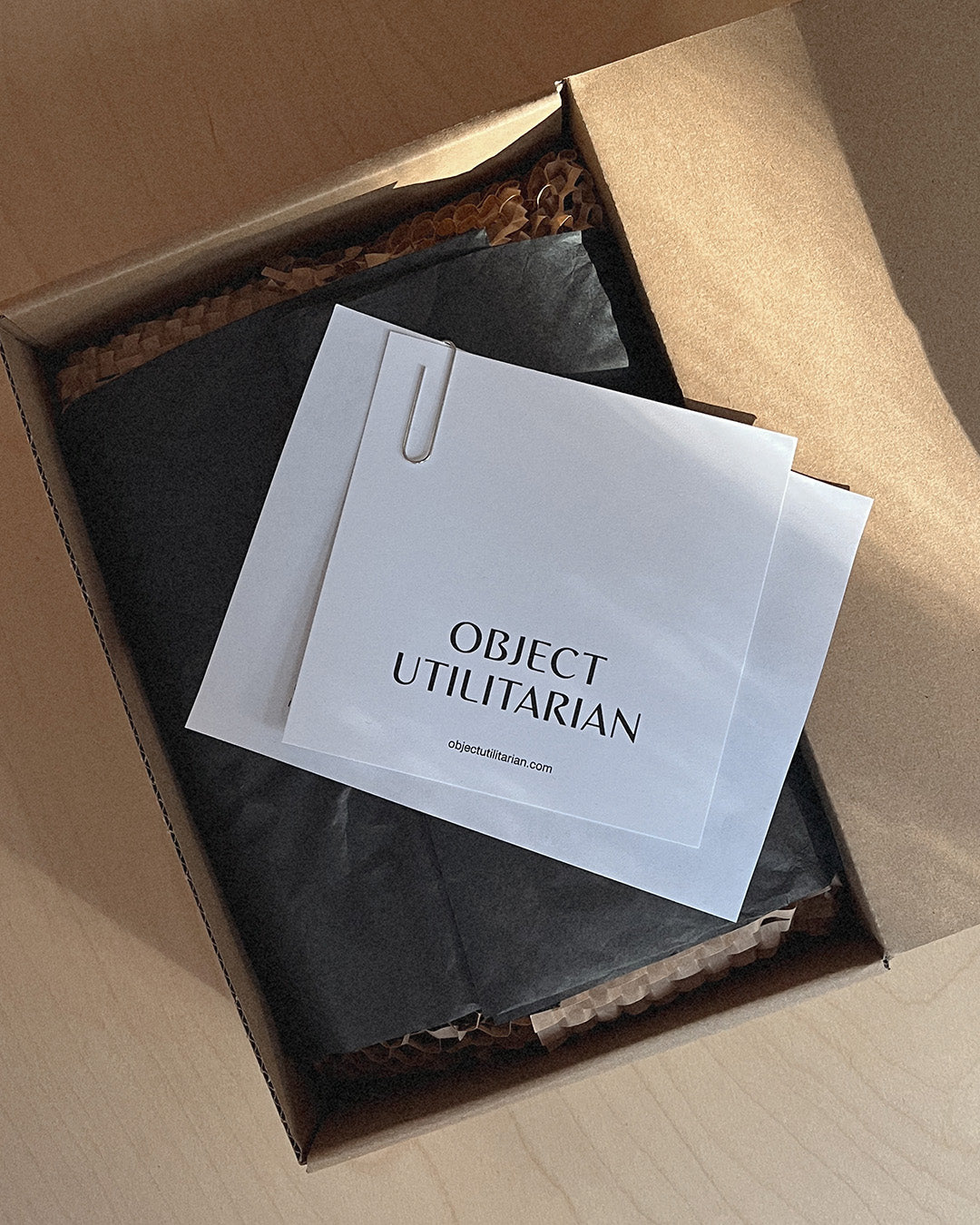 Product packaging and card with "Object Utilitarian" logo, on a wooden surface.