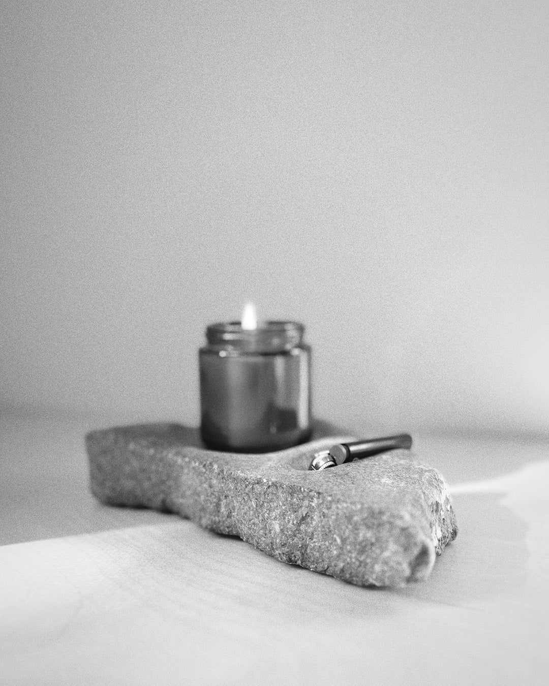 Front: gray stone sculpture, raw edges, carved spaces for—and holding—lighter and jar candle. 