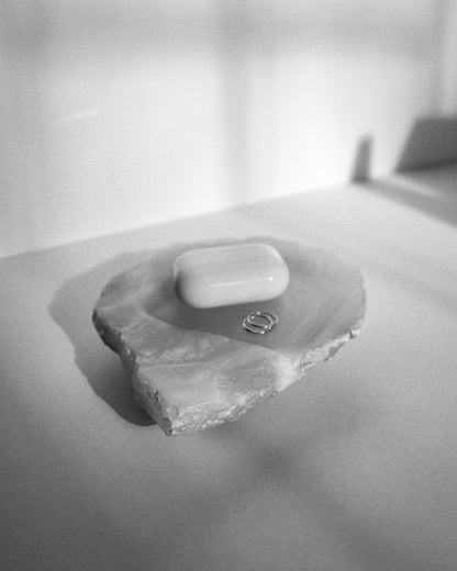 Angled view: white translucent alabaster tray, organic shape, raw edges holding jewelry and earbuds.