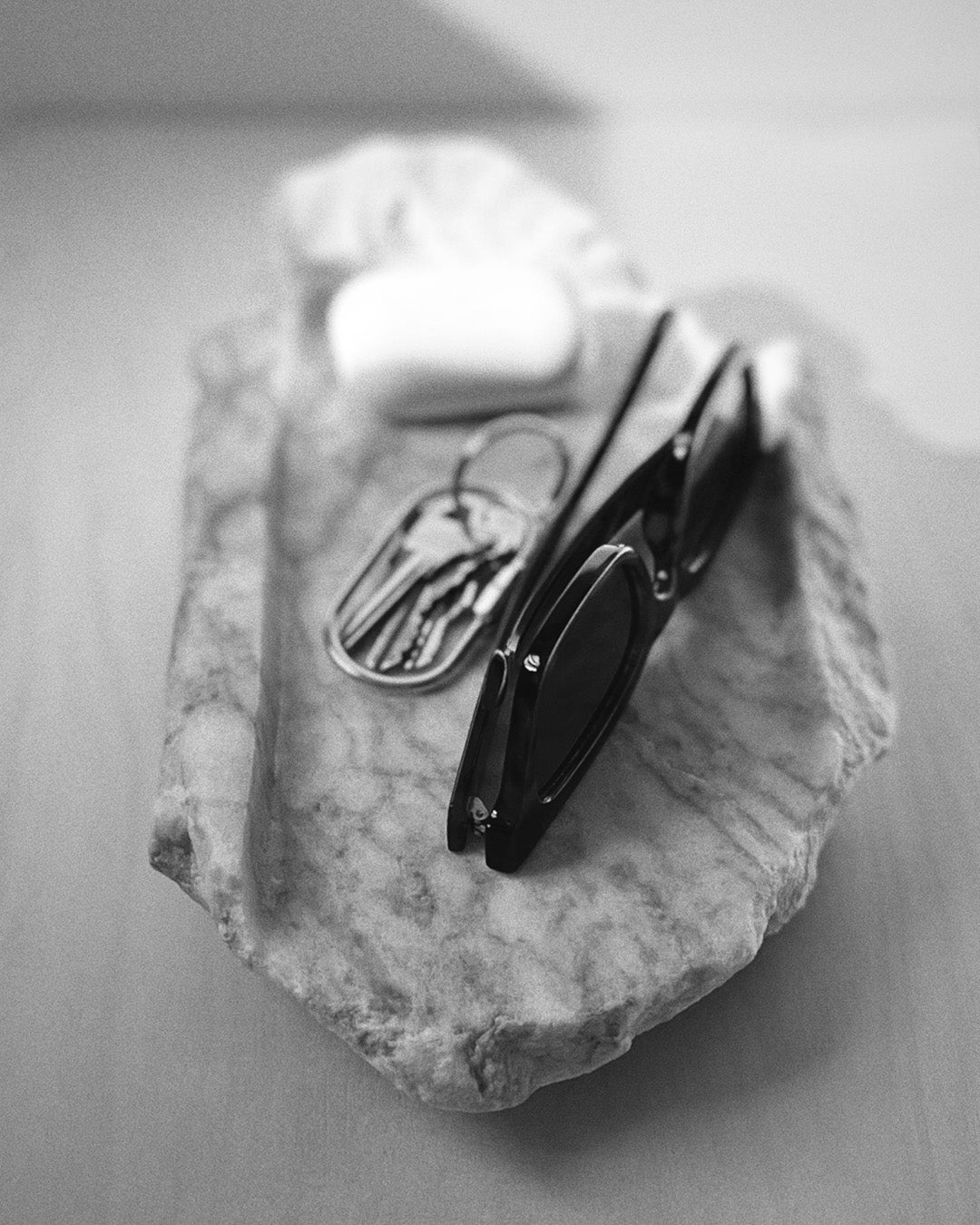 Front-on: organic-shaped gray streaked alabaster tray, holding sunglasses, keys and earbuds.