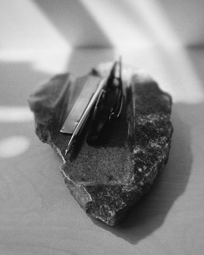 Front-on: organic-shaped dark stone tray, raw edges, holding sunglasses, pen, letter opener.